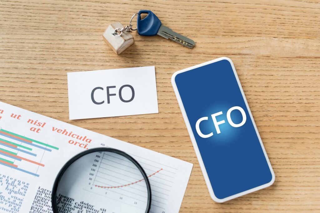 top view of magnifier near charts, paper with cfo lettering near smartphone cfo lettering on screen
